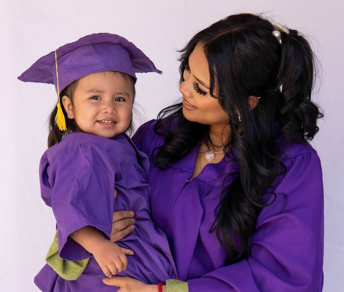 Mother and toddler in matching purple graduation gowns.
