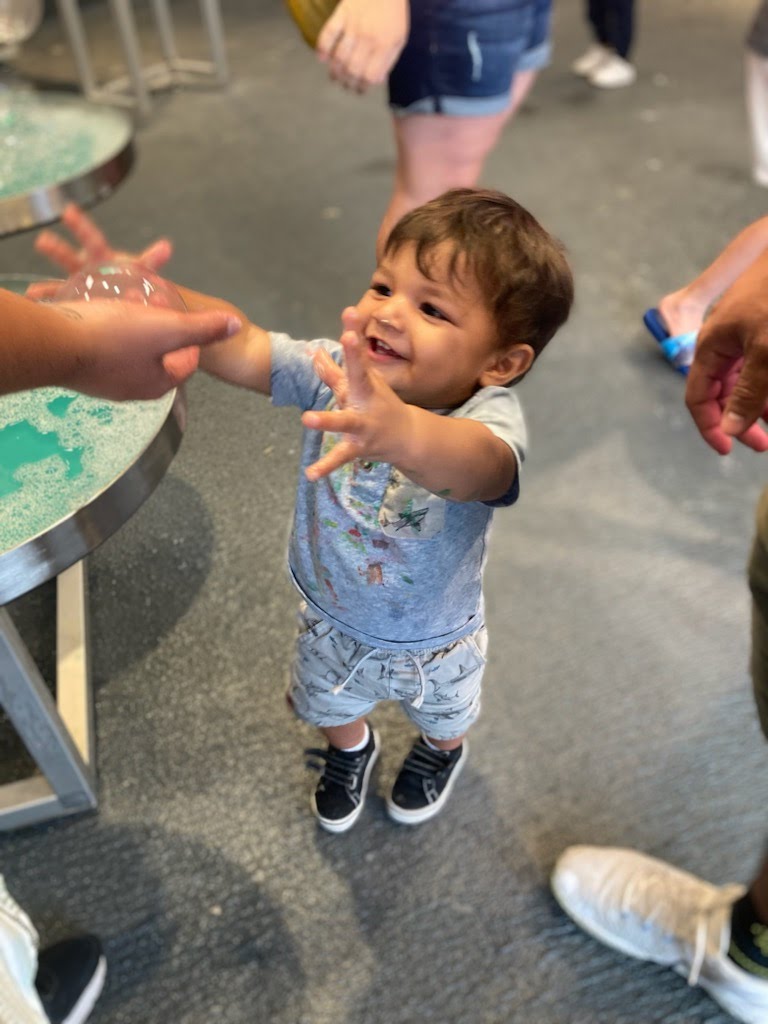 Smiling toddler reaches for a bubble.