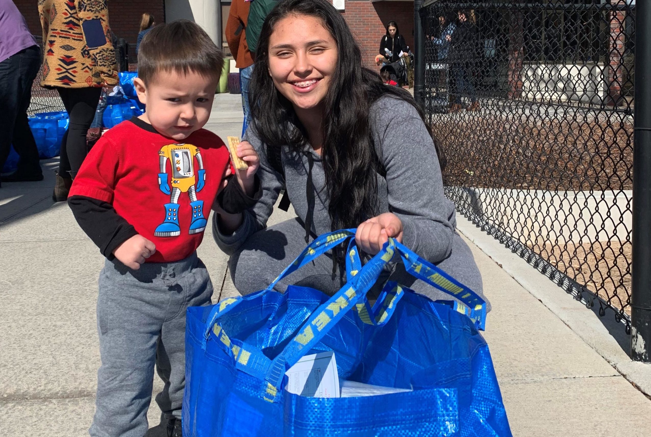 Smiling woman and child with IKEA bag outdoors.