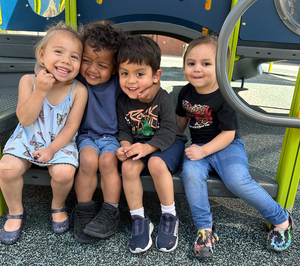 Four smiling kids sitting on playground equipment.