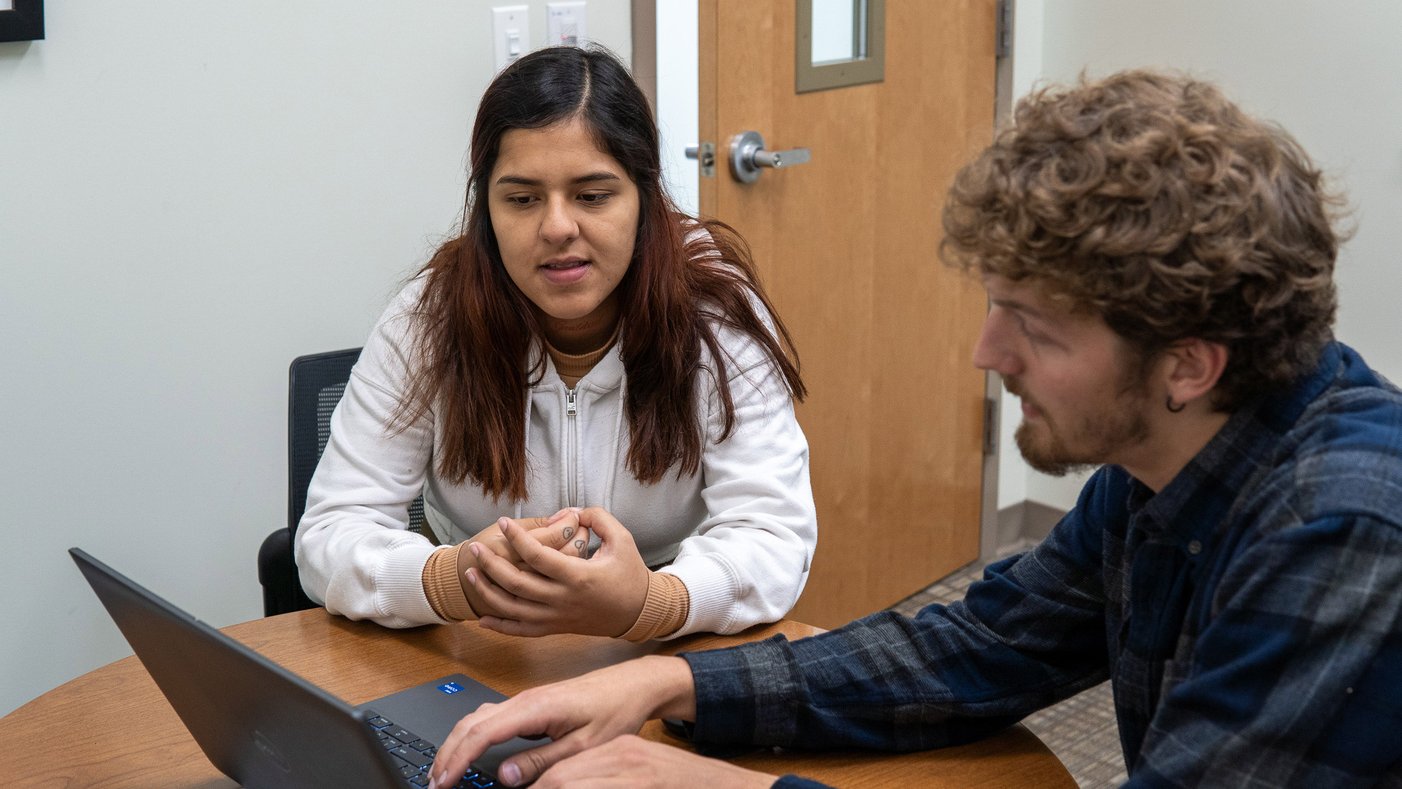 Two people collaborating on laptop at desk.