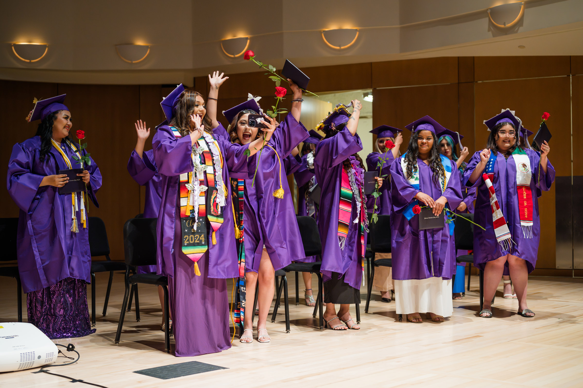 Graduates celebrating in purple gowns with roses.
