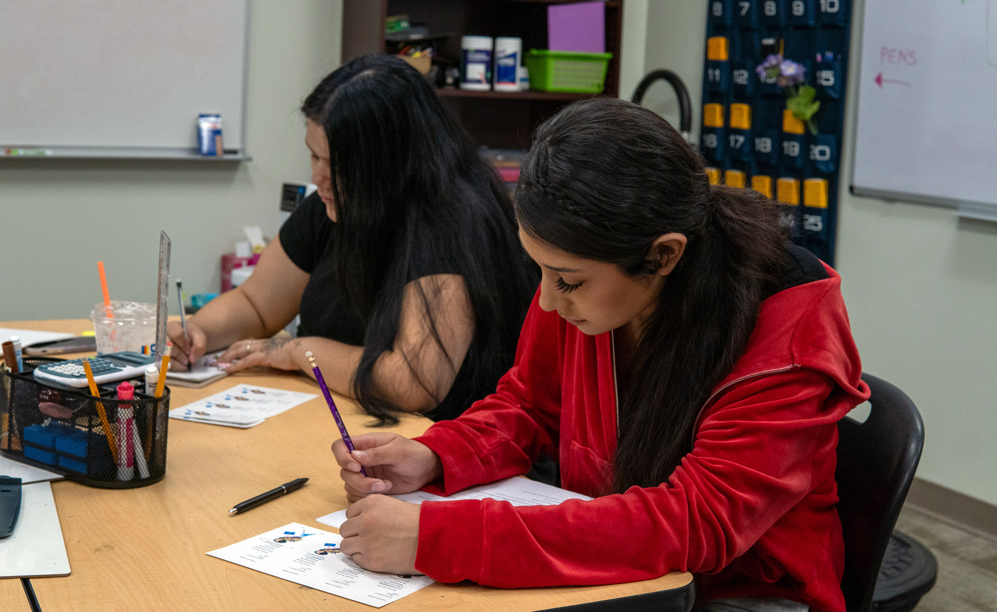 Students writing at a classroom table.