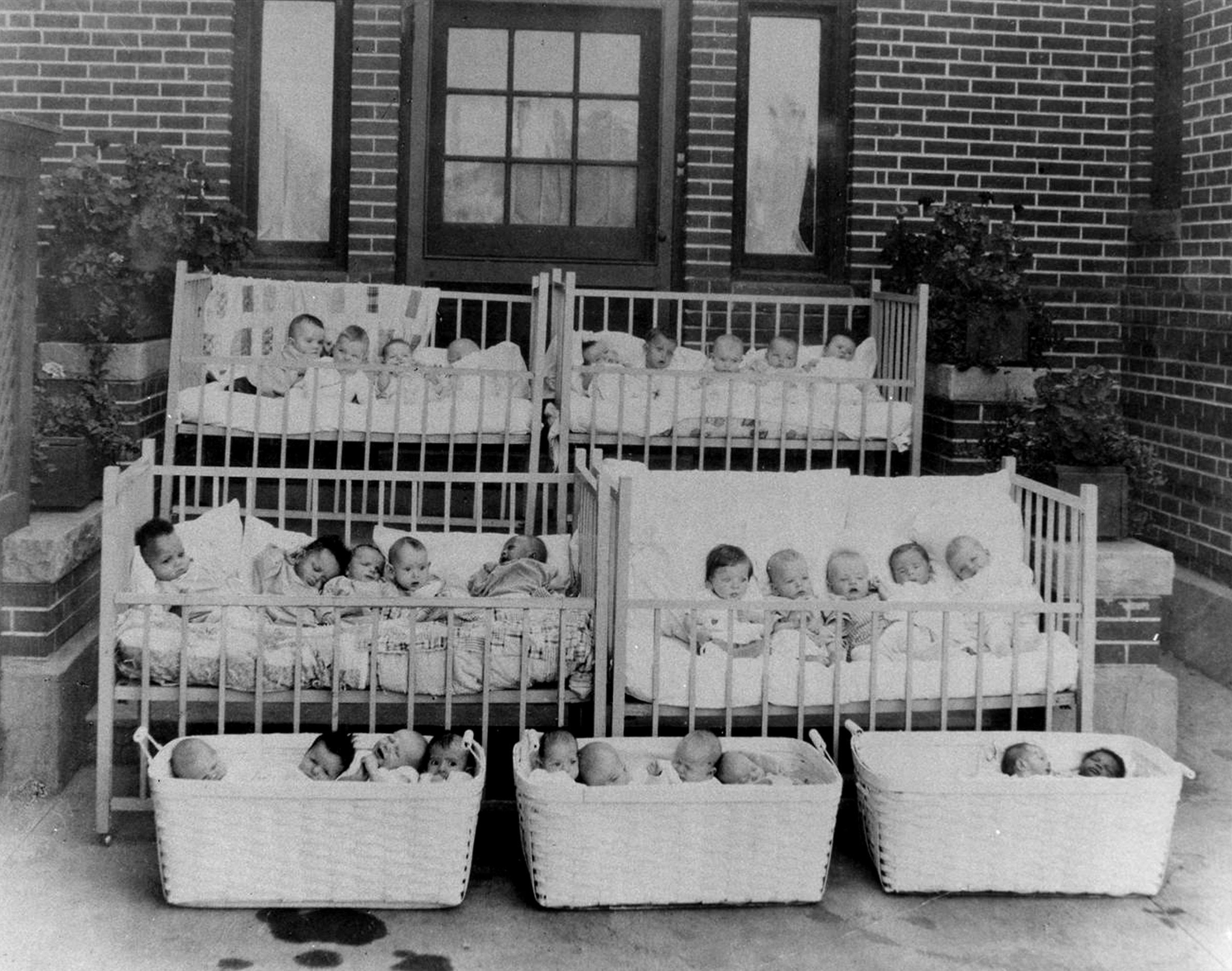 Multiple babies in cribs and baskets outdoors.