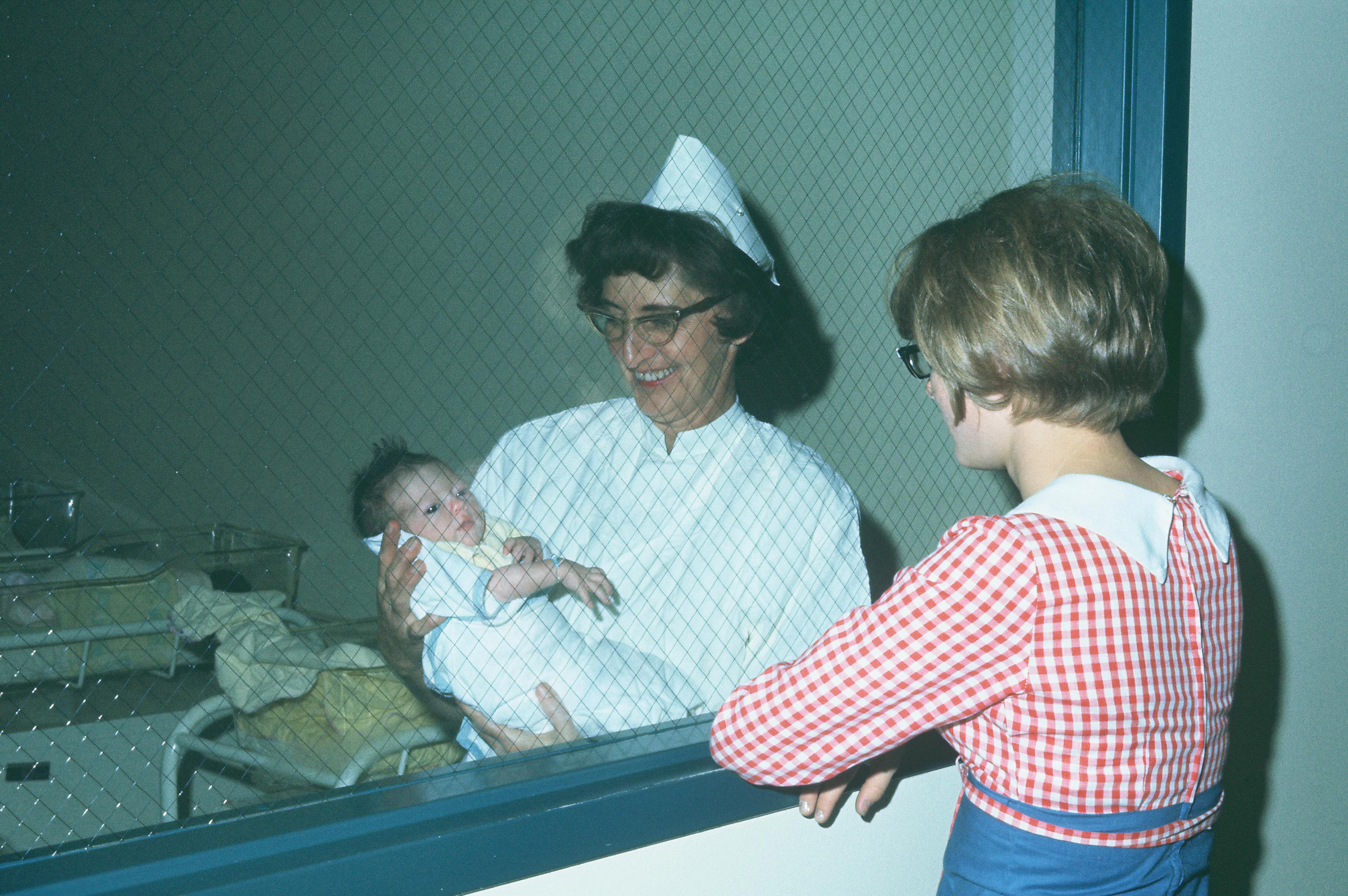 Nurse showing baby to woman through glass window.