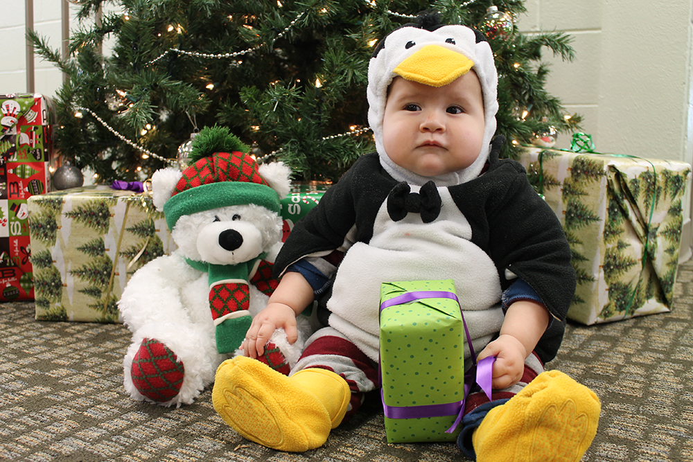 Baby in penguin costume with Christmas presents.