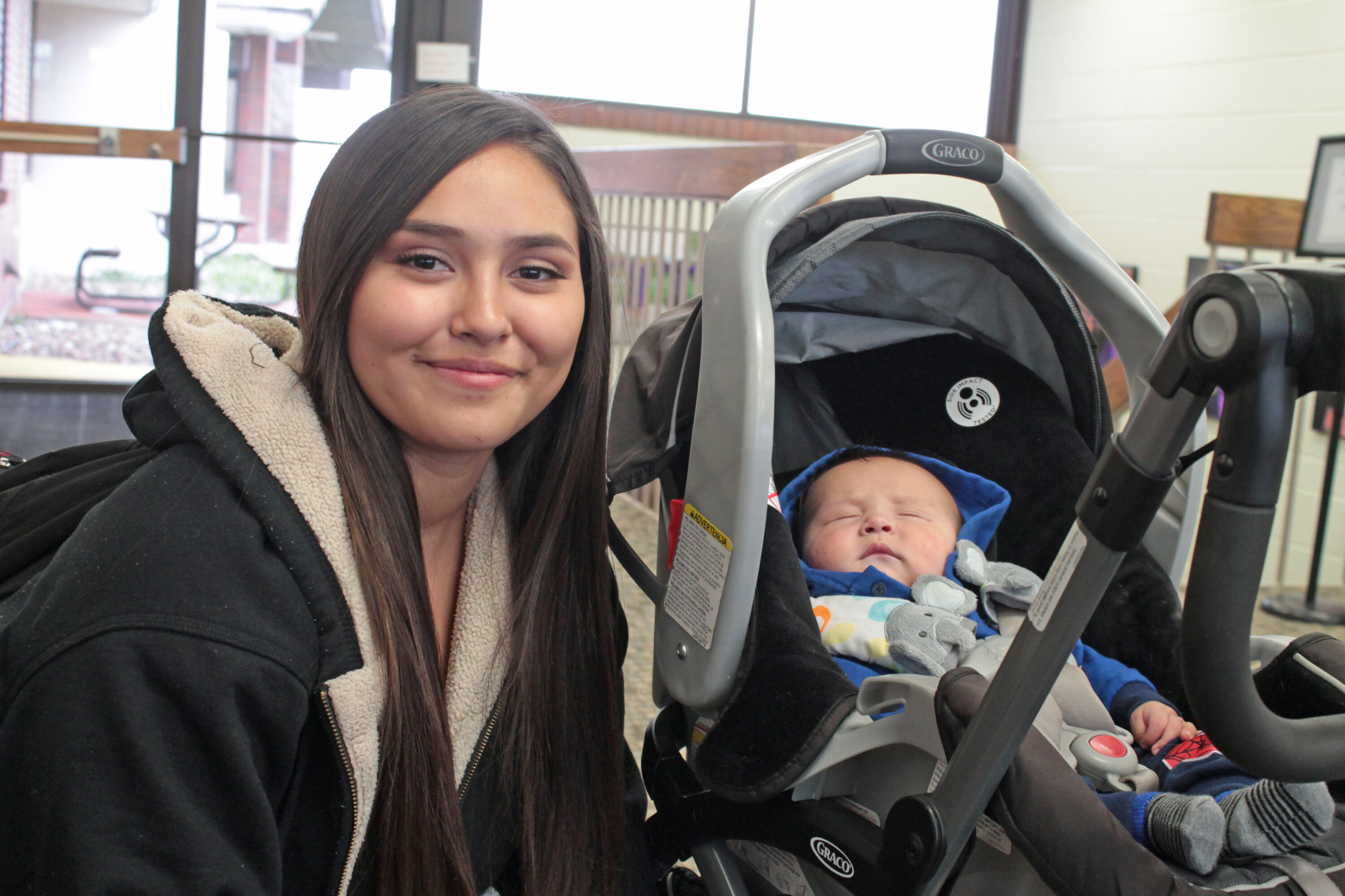 Woman smiling beside a sleeping baby in stroller.