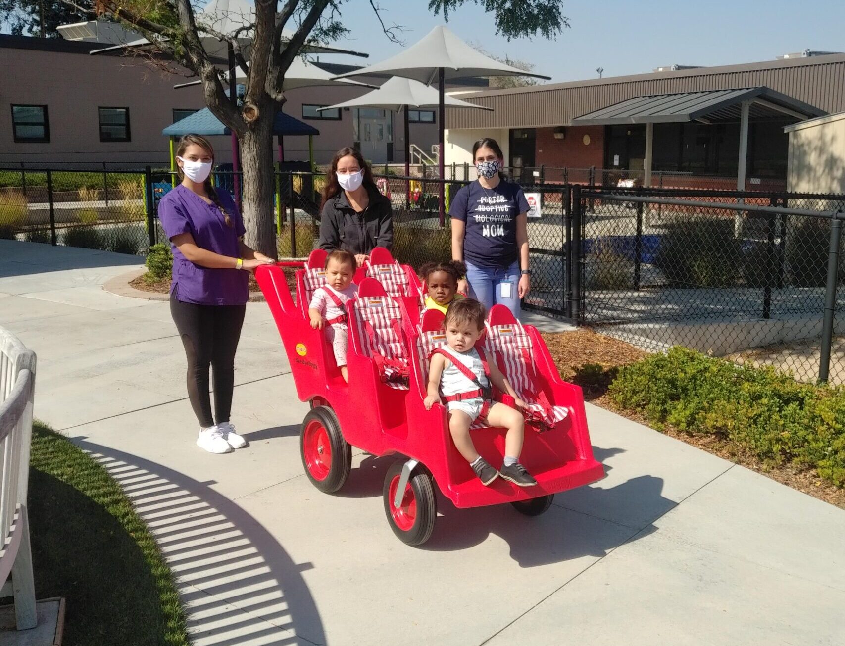 Caregivers with toddlers in red stroller outdoors.