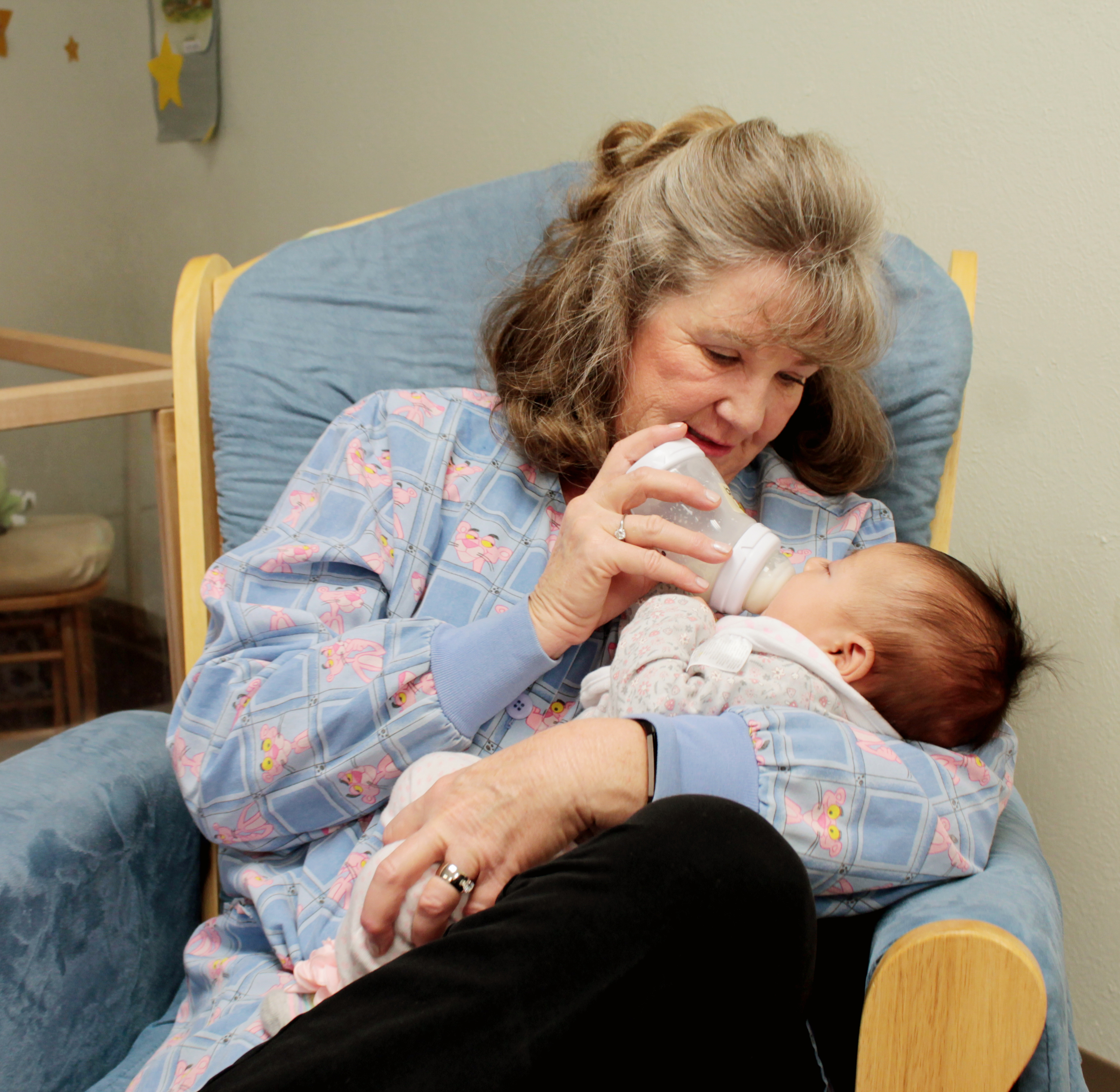 Woman bottle-feeding a baby in chair.
