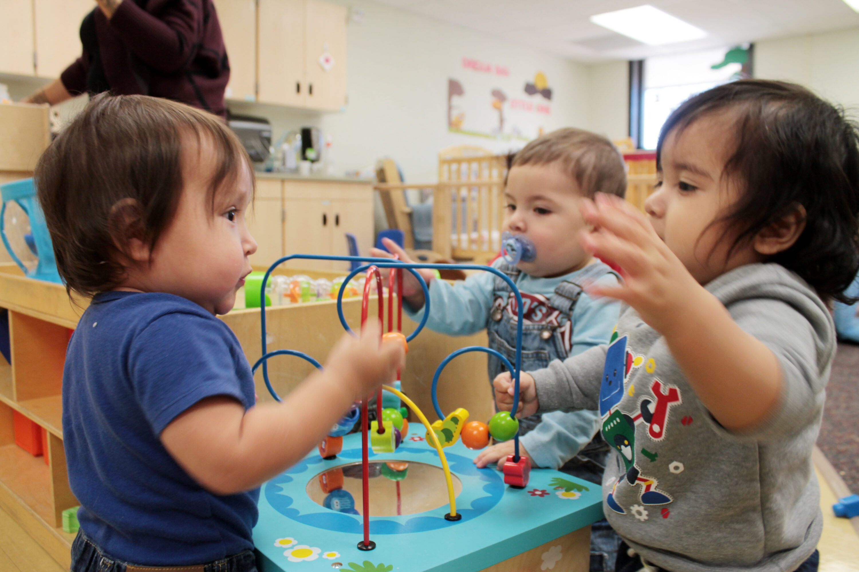 Toddlers playing with colorful bead maze toy.