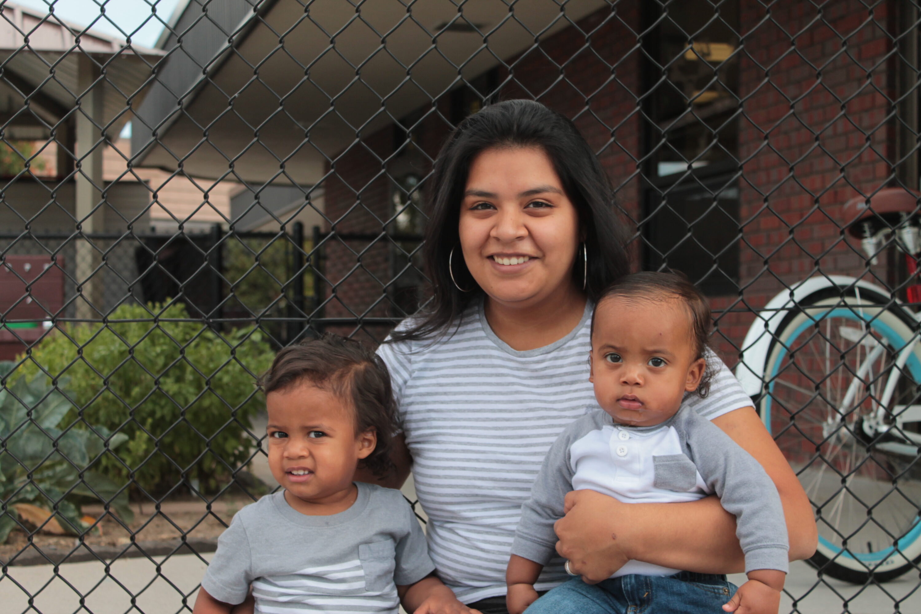 Smiling woman with two children near fence.