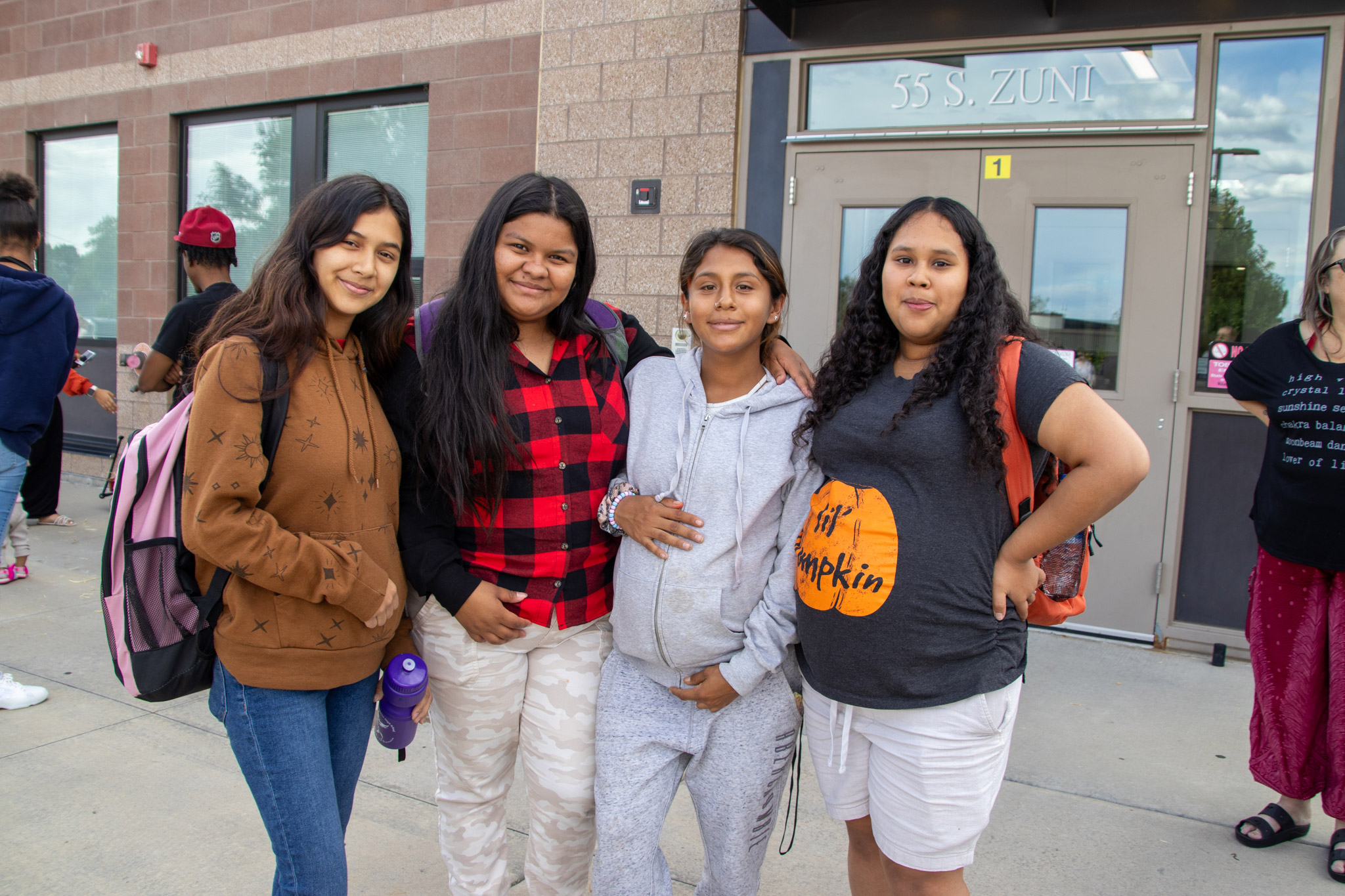 Four friends smiling outside a school entrance.